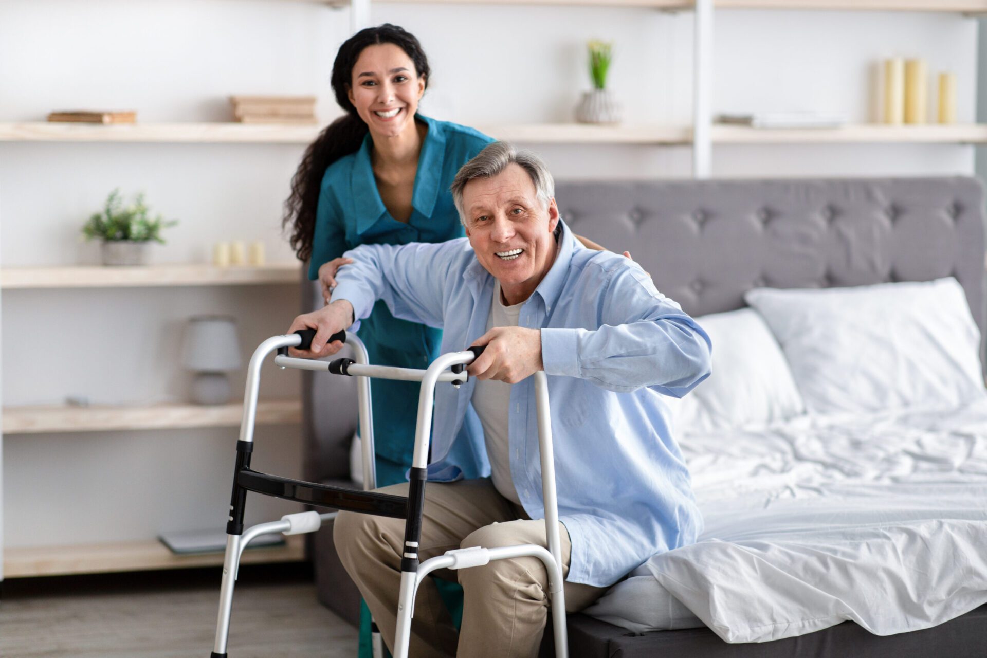Movement and Mobility Female nurse helping elderly male with walking frame stand up from bed at home. Professional care for disabled patients